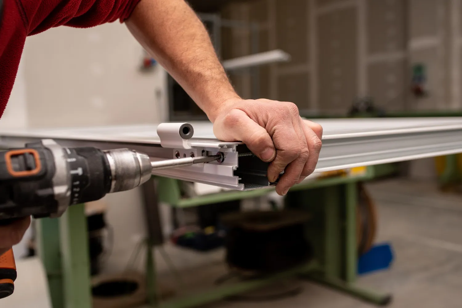 Technician drilling hardware prep into a steel door on a fabrication table