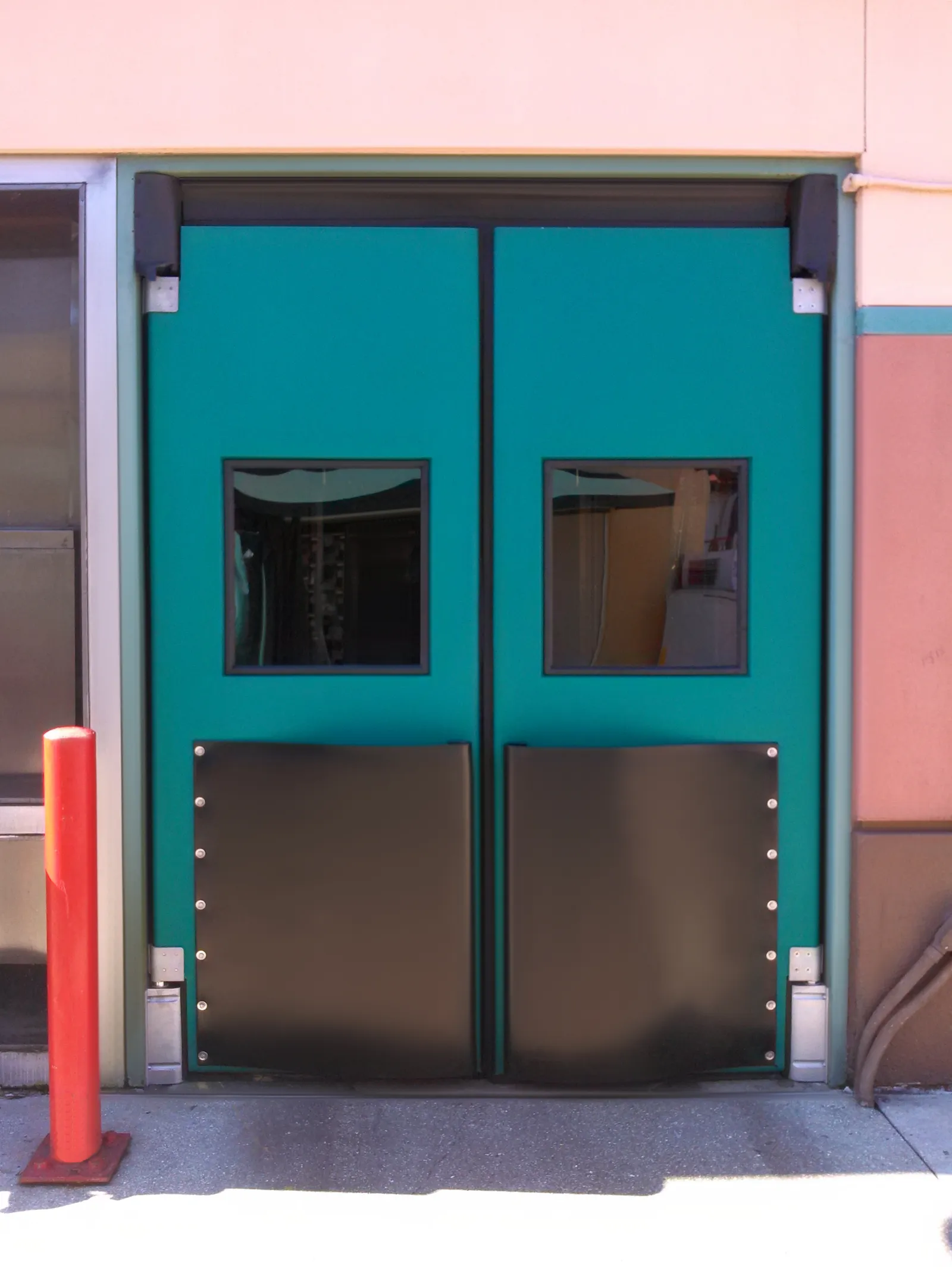 Teal impact traffic double doors with vision windows and kick plates at a service entrance
