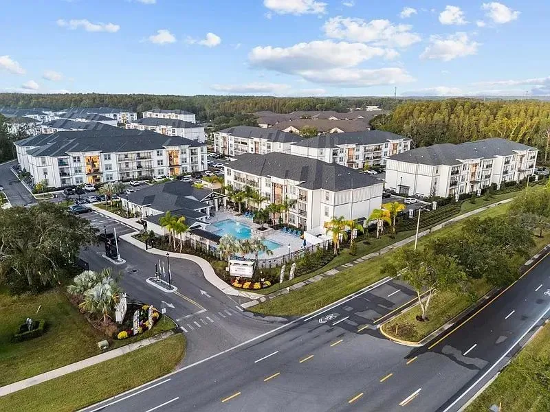 Aerial view of a garden-style apartment community with three-story buildings, a pool and a landscaped entry drive in the Tampa, Florida area