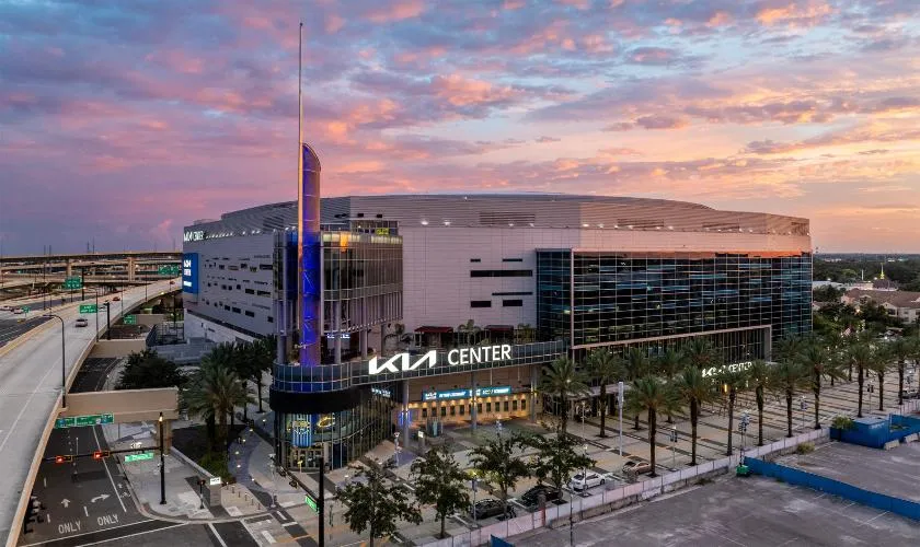 Kia Center arena in downtown Orlando, Florida at dusk, with its illuminated Kia Center sign and glass facade