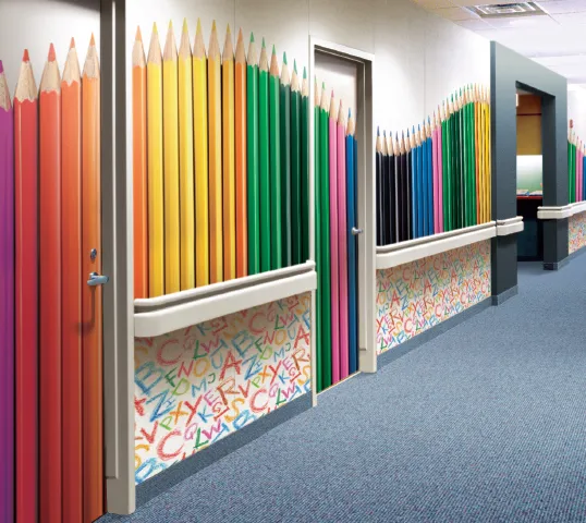 School corridor with an Acrovyn wall covering printed with oversized colored pencils above a handrail