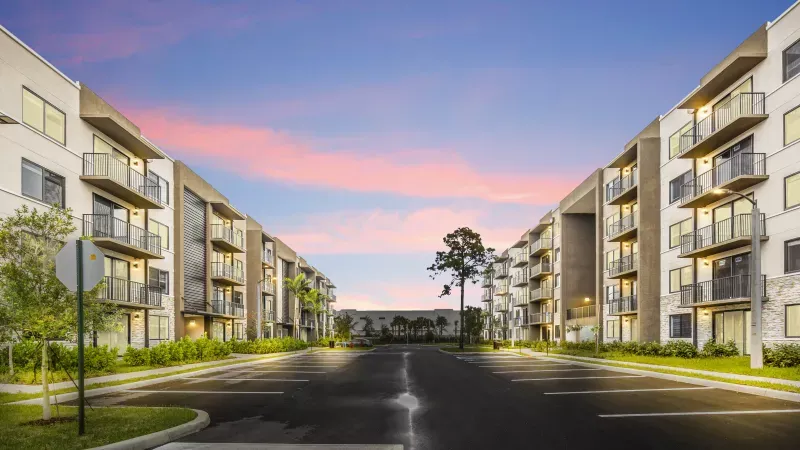 Four-story Pine Ridge apartment buildings with private balconies facing a parking court at dusk in West Palm Beach, Florida