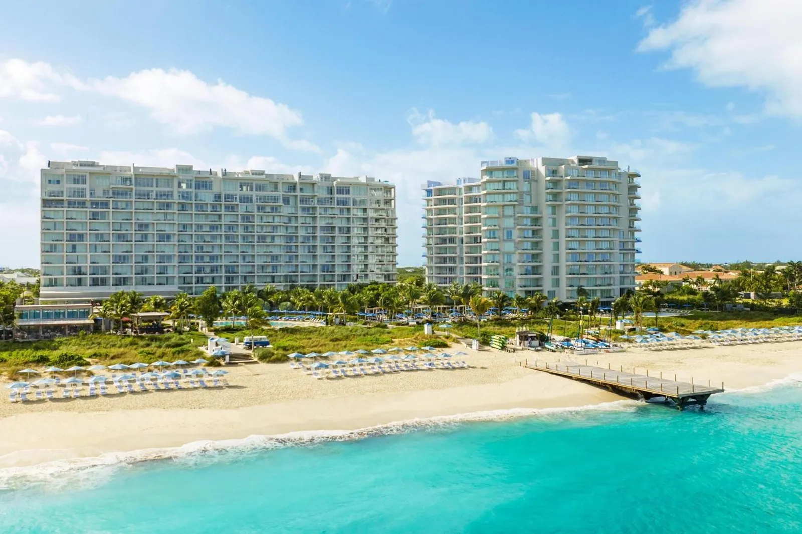 The Ritz-Carlton, Turks & Caicos resort towers on Grace Bay Beach in Providenciales, with turquoise water and a pier in the foreground