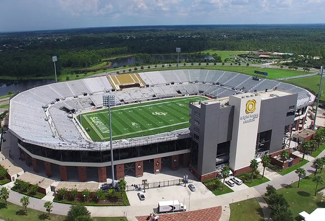 Aerial view of the UCF football stadium in Orlando, Florida, with the multi-level premium seating tower rising beside the field