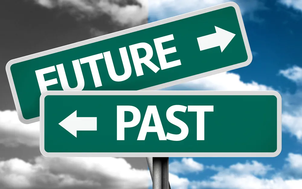 Green street signs pointing to Future and Past against a cloudy blue sky
